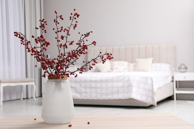 Photo of Hawthorn branches with red berries on wooden table in bedroom, space for text