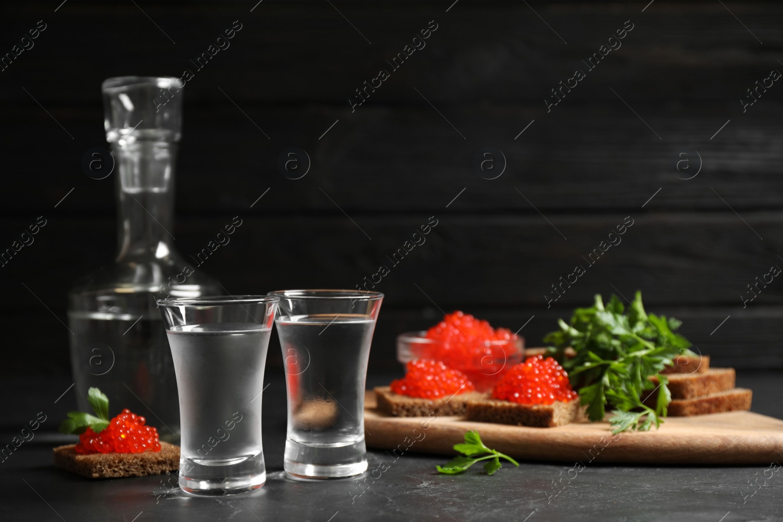 Photo of Cold Russian vodka and sandwiches with red caviar on black table