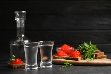 Photo of Cold Russian vodka and sandwiches with red caviar on black table