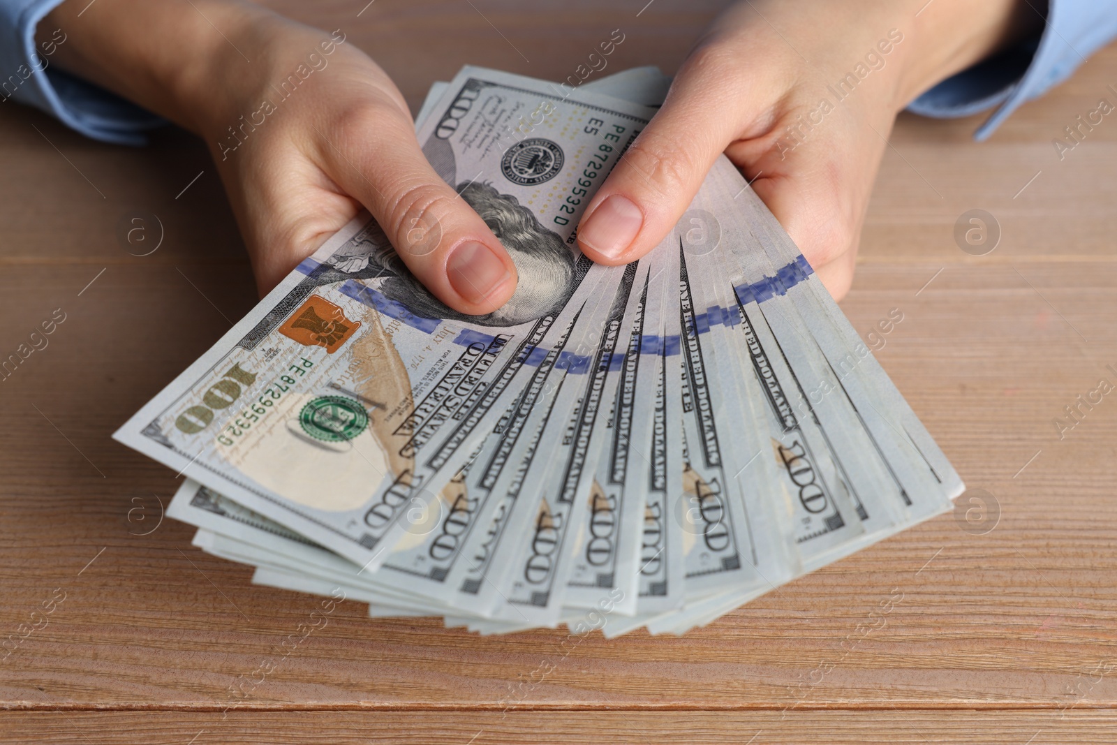 Photo of Money exchange. Woman holding dollar banknotes at wooden table, closeup