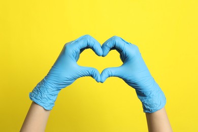 Photo of Doctor in medical gloves making heart with hands on yellow background, closeup