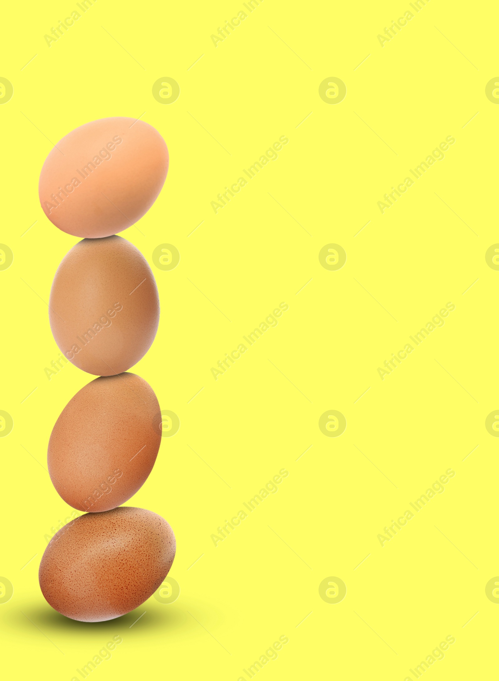 Image of Stacked fresh chicken eggs against light yellow background. Space for text