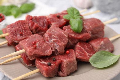 Wooden skewers with cut fresh beef meat, basil leaves and spices on beige plate, closeup