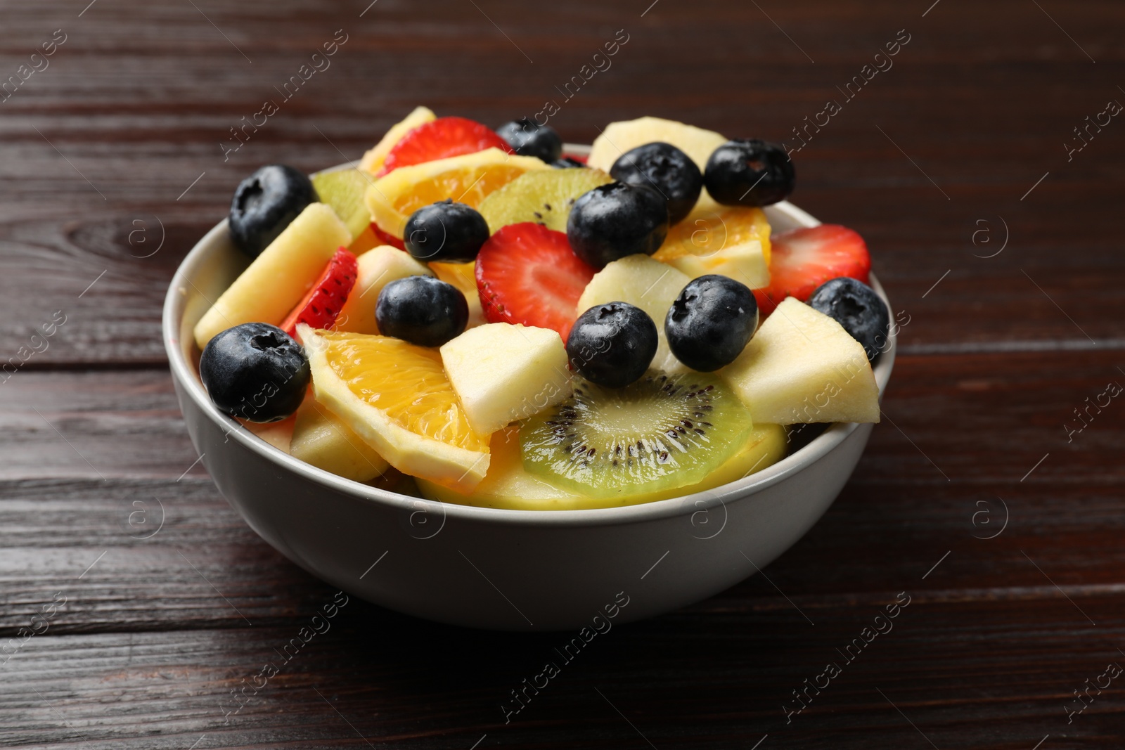 Photo of Tasty fruit salad in bowl on wooden table, closeup