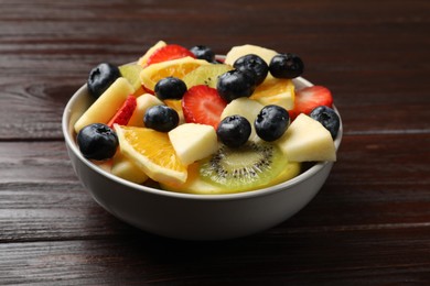 Tasty fruit salad in bowl on wooden table, closeup