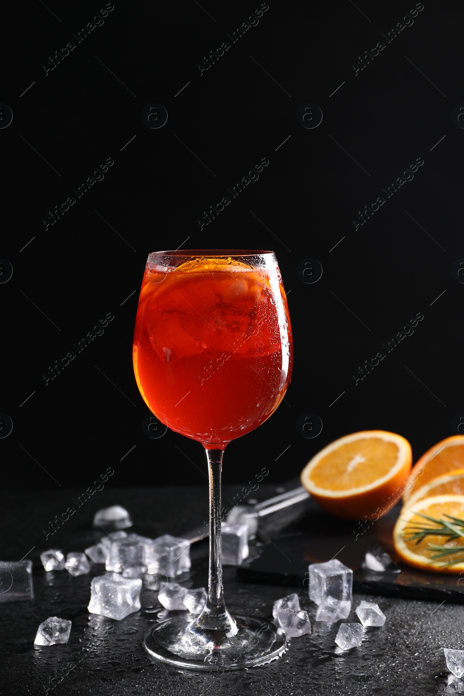 Photo of Glass of tasty Aperol spritz cocktail with orange slices and ice cubes on table against black background