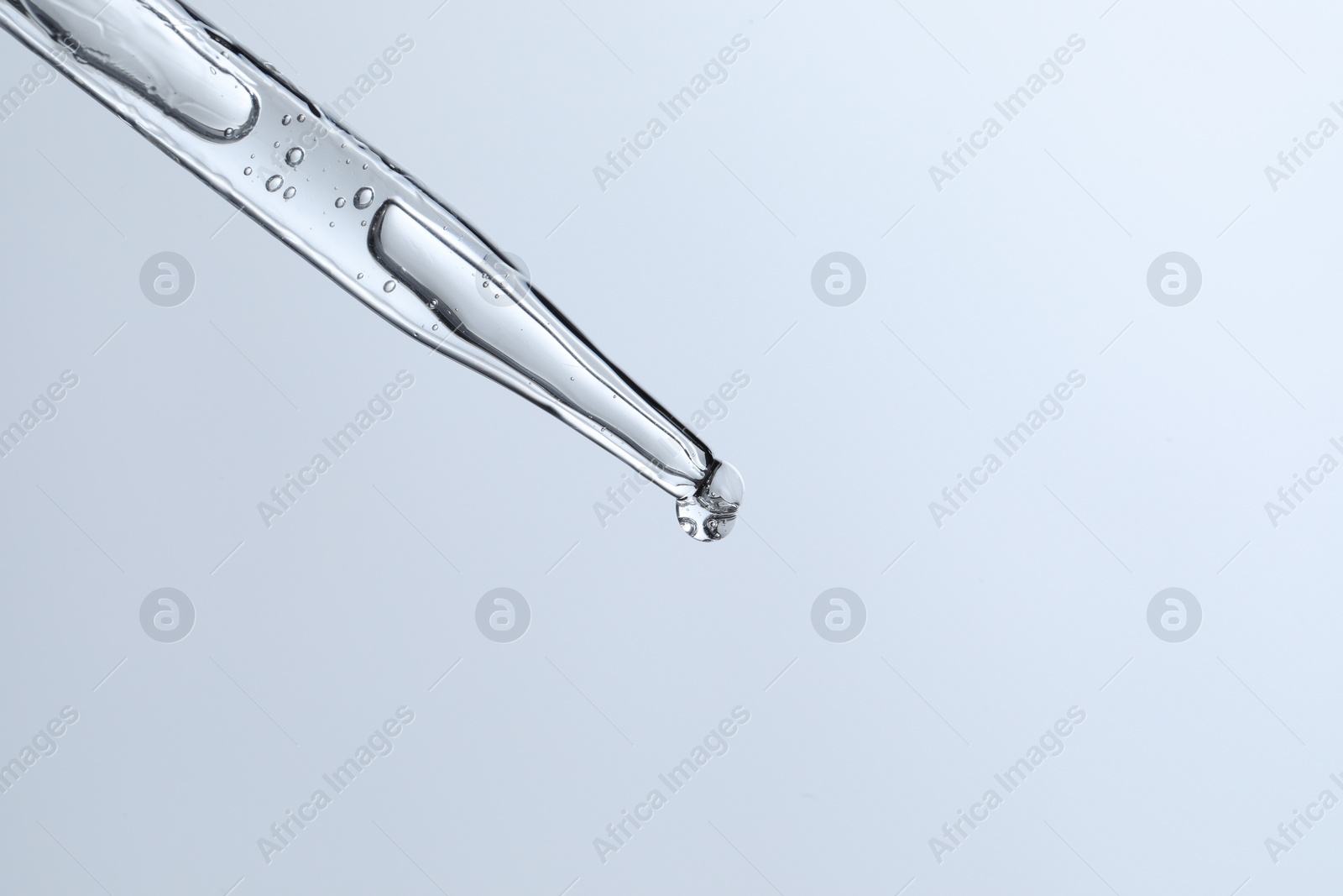 Photo of Dripping liquid from pipette on light blue background, closeup. Space for text