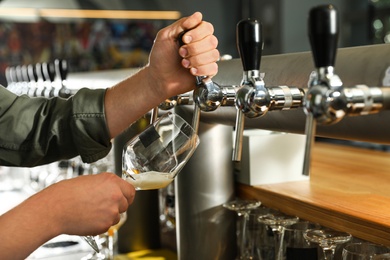 Photo of Bartender pouring fresh beer into glass in pub, closeup