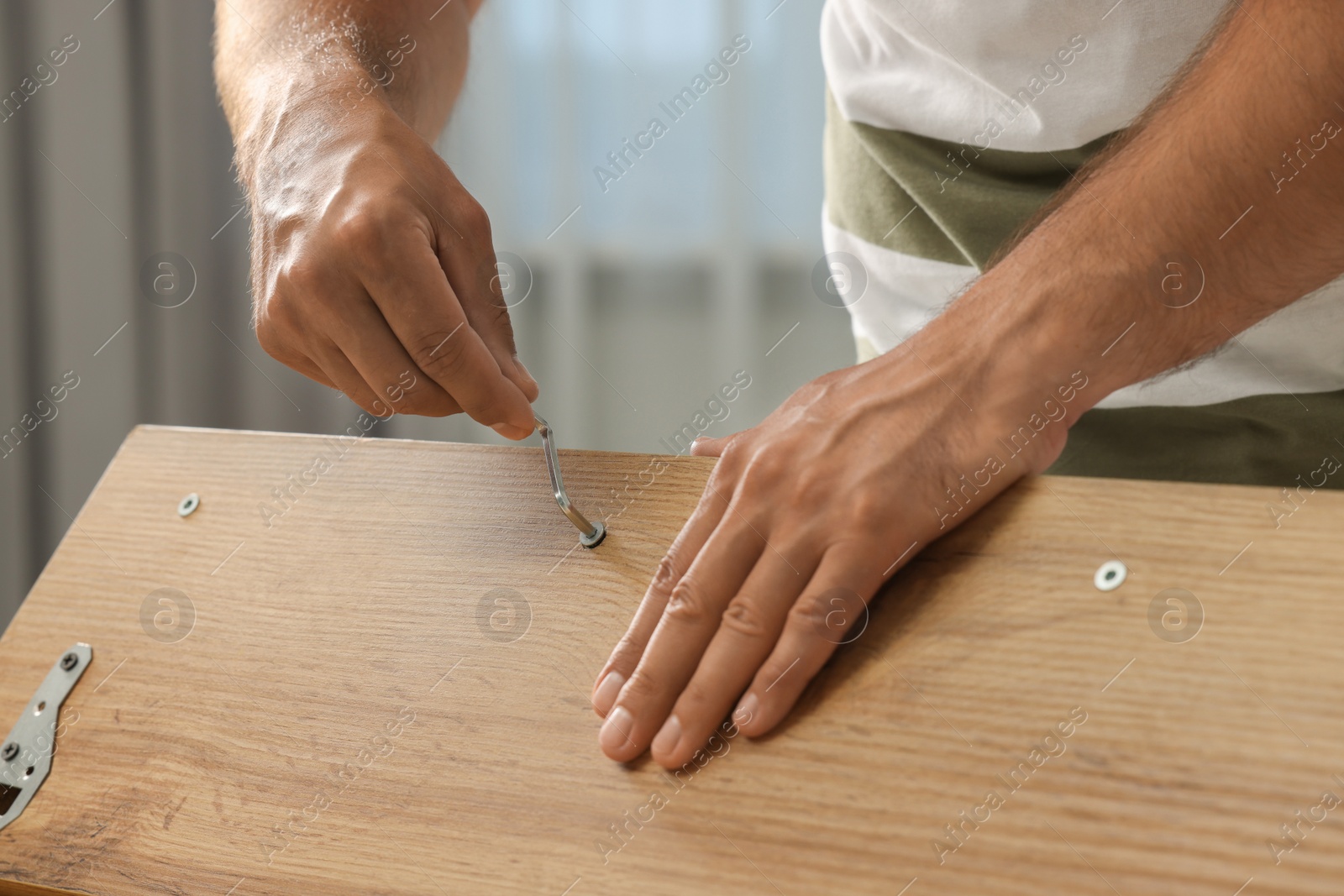Photo of Man with hex key assembling furniture indoors, closeup