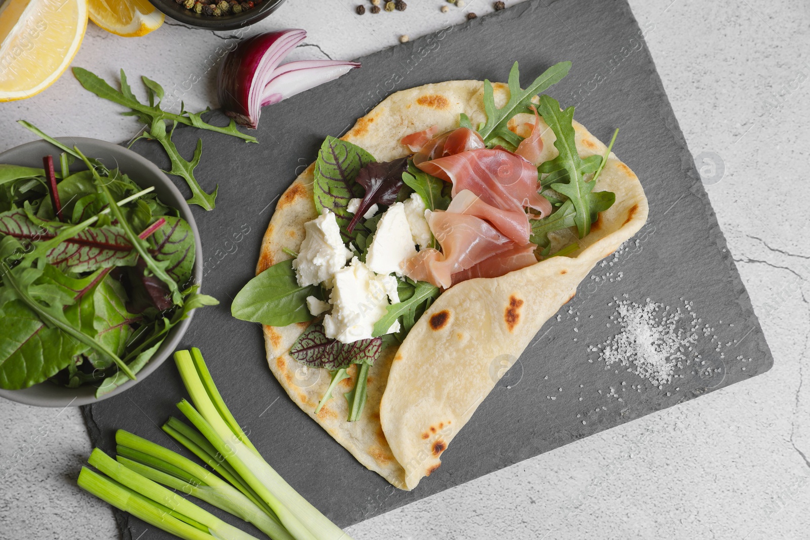 Photo of Delicious pita wrap with jamon, cheese cream and greens on light gray table, flat lay