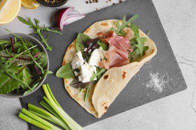 Delicious pita wrap with jamon, cheese cream and greens on light gray table, flat lay