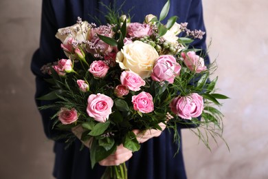 Woman with bouquet of beautiful roses on beige background, closeup