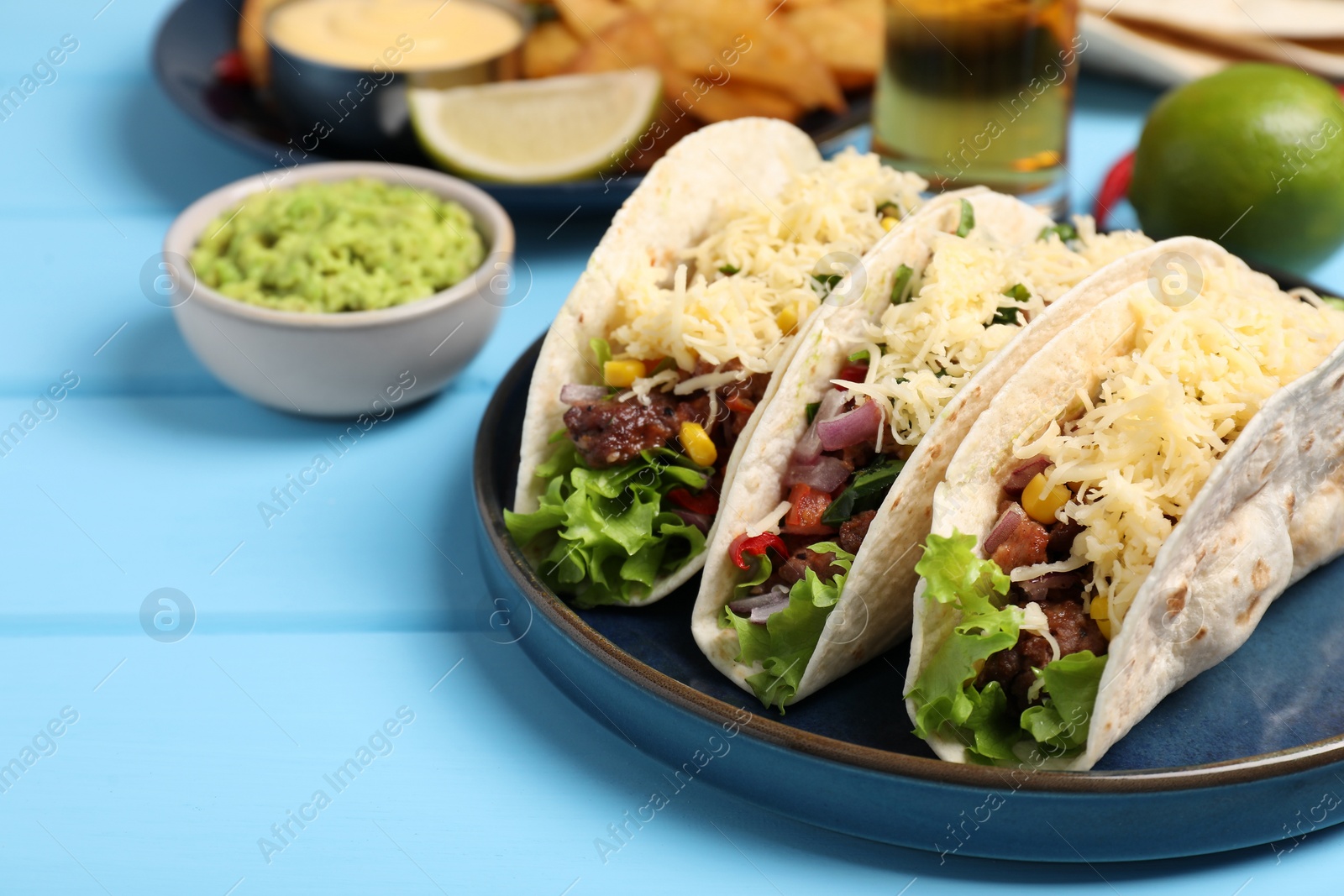 Photo of Delicious tacos with meat and vegetables on light blue wooden table, closeup