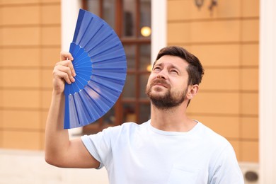 Photo of Man with hand fan suffering from heat outdoors