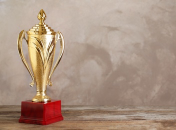 Photo of Golden trophy cup on wooden table against light brown background. Space for text