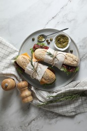 Photo of Delicious sandwiches with bresaola, cheese and lettuce served on white marble table, flat lay