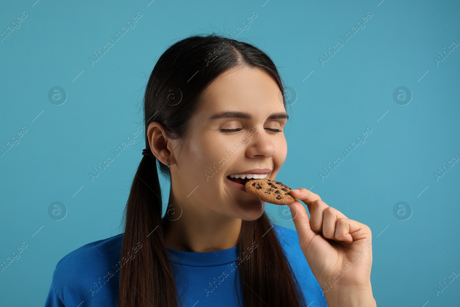 Photo of Young woman with chocolate chip cookie on light blue background