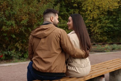 Photo of Young couple spending time together on wooden bench in autumn park, back view