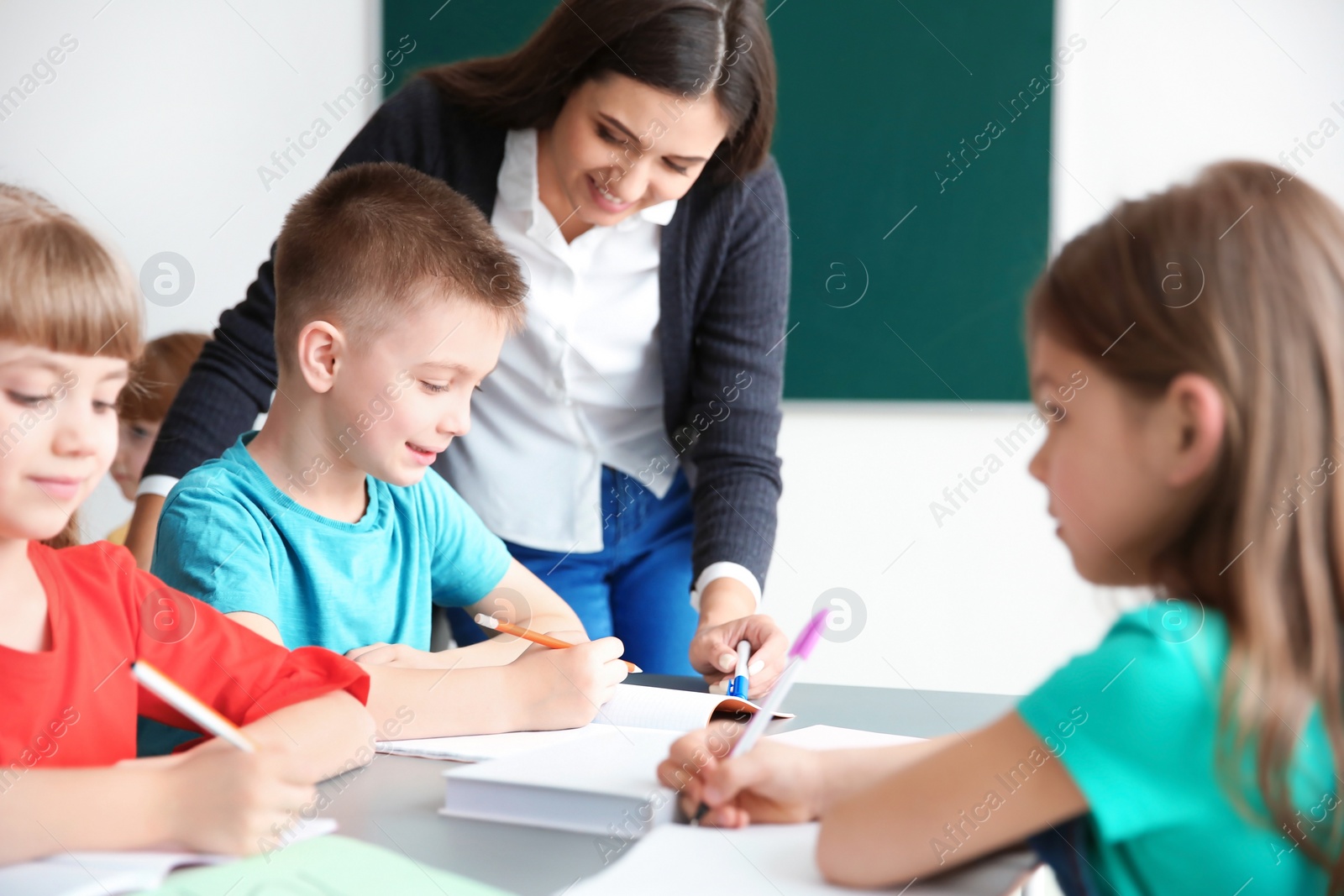 Photo of Female teacher helping boy with his task in classroom at school