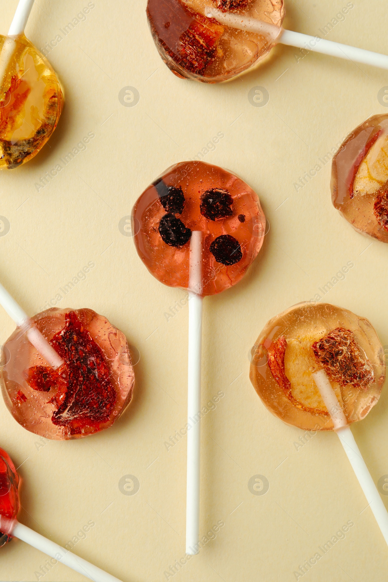 Photo of Sweet colorful lollipops with berries on beige background, flat lay