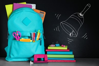 Image of Backpack full of stationery near blackboard with drawn school bell