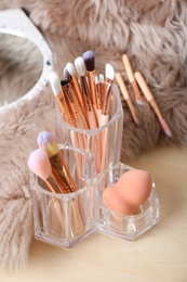 Organizer with set of professional makeup brushes on wooden table