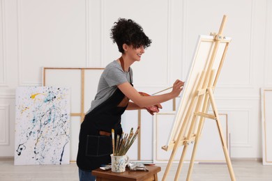 Photo of Young woman painting on easel with canvas in studio