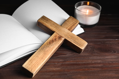 Cross, Bible and burning candle on wooden background, closeup. Christian religion