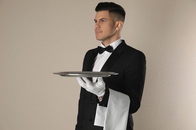 Photo of Handsome butler with tray on beige background