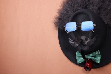 Man's face made of artificial mustache, sunglasses and hat on brown background, top view. Space for text