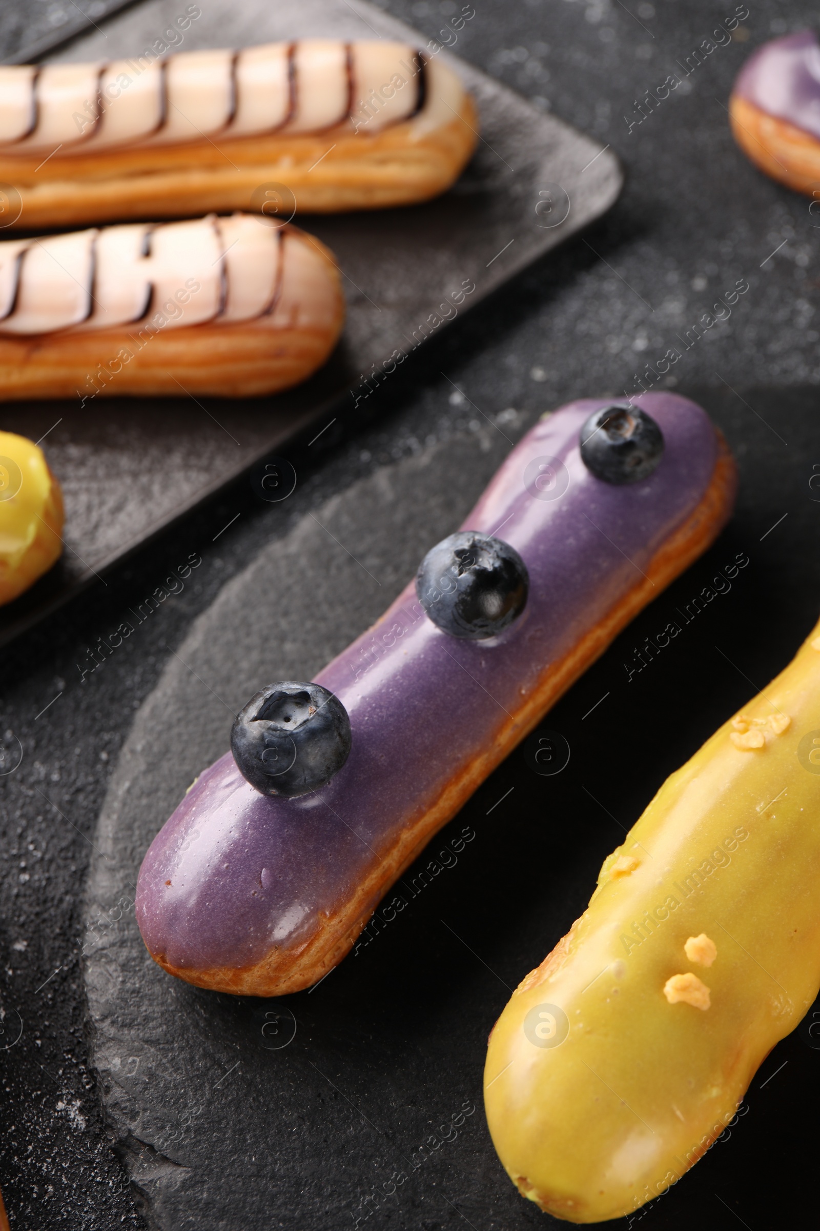 Photo of Different tasty glazed eclairs on dark textured table, above view