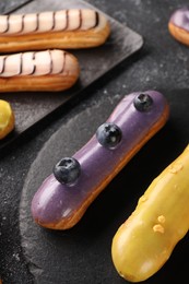 Different tasty glazed eclairs on dark textured table, above view