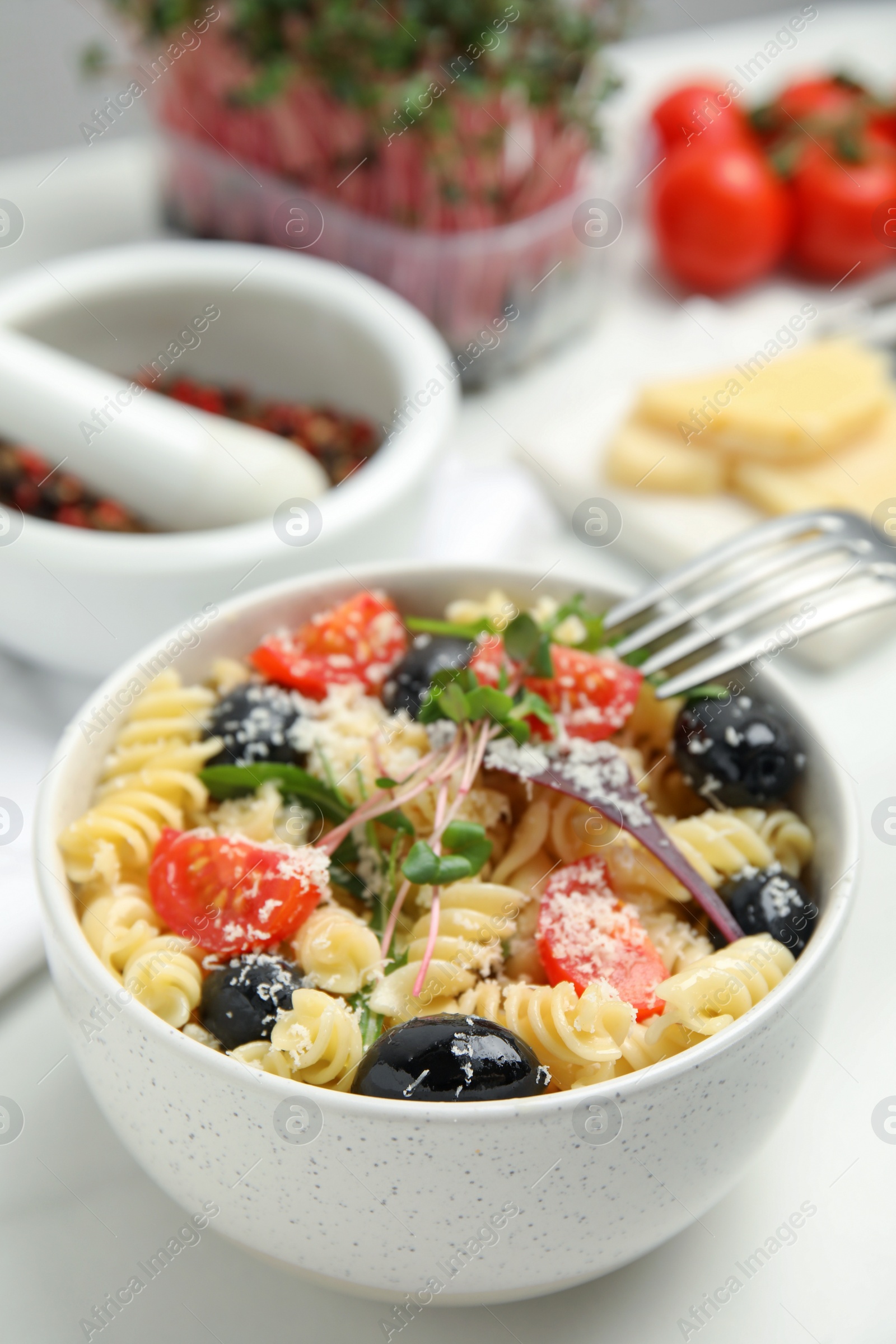 Photo of Bowl of delicious pasta with tomatoes, olives and cheese on white table, closeup