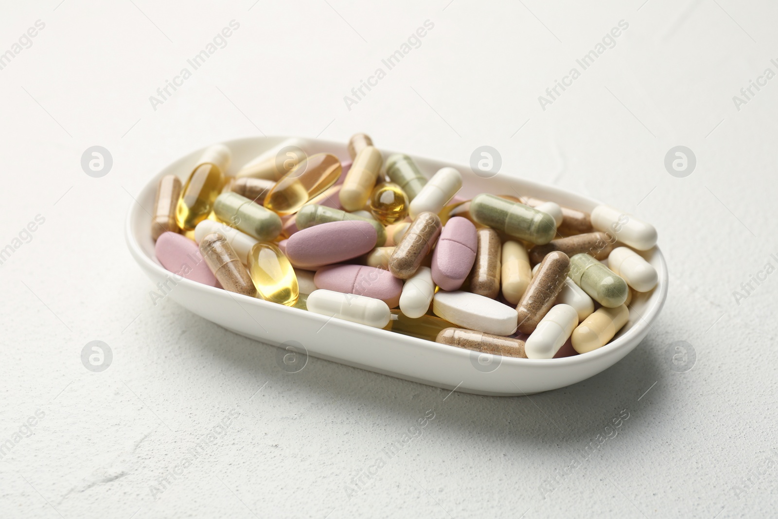 Photo of Different vitamin capsules in bowl on white wooden table