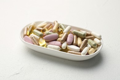 Different vitamin capsules in bowl on white wooden table