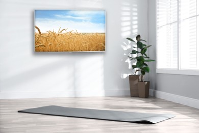 Image of Modern wide screen TV on white wall in room with yoga mat