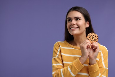 Young woman with chocolate chip cookie on purple background, space for text