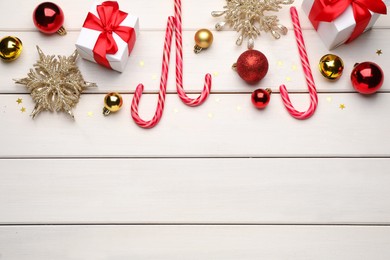 Flat lay composition with tasty candy canes and Christmas decor on white wooden table, space for text