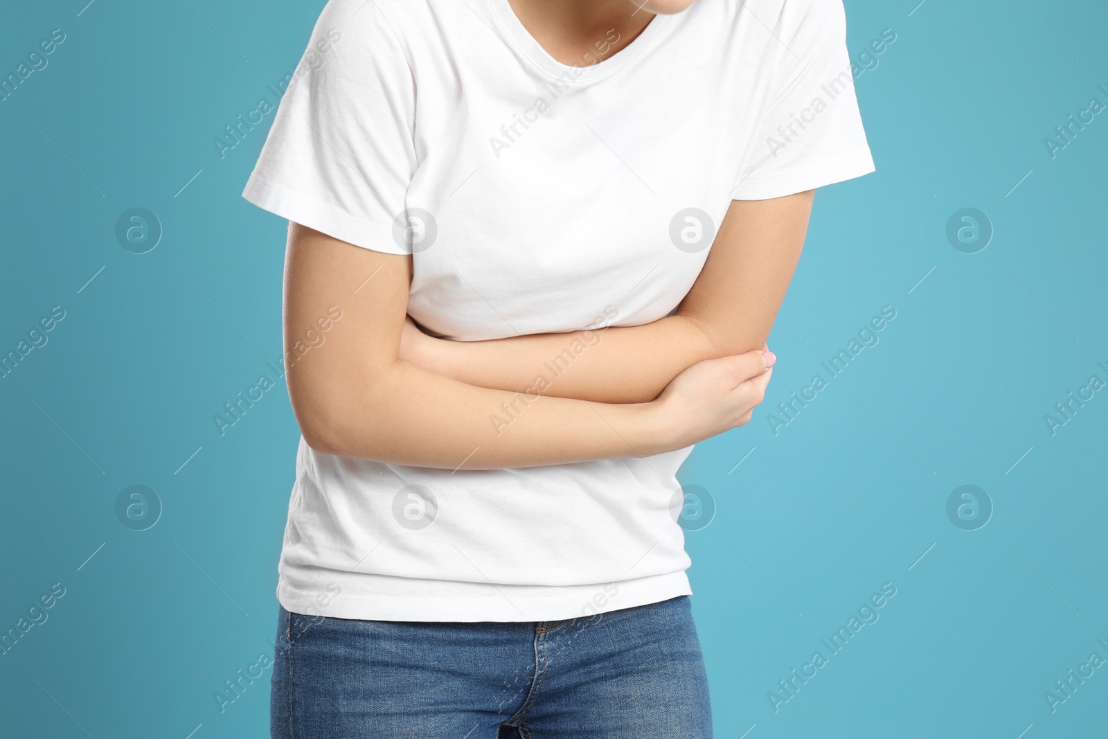 Photo of Young woman suffering from stomach ache on light blue background, closeup. Food poisoning