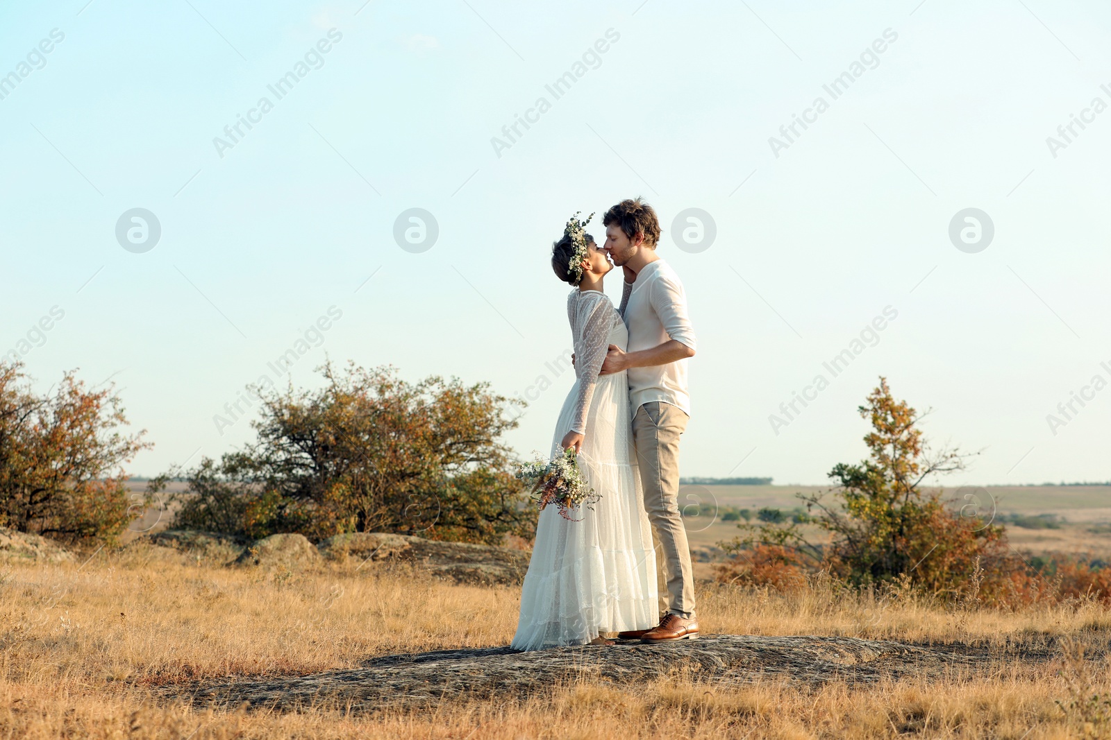 Photo of Happy newlyweds with beautiful field bouquet outdoors