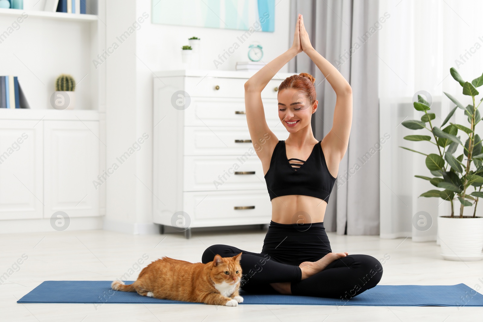 Photo of Beautiful woman with cute red cat practicing yoga on mat at home