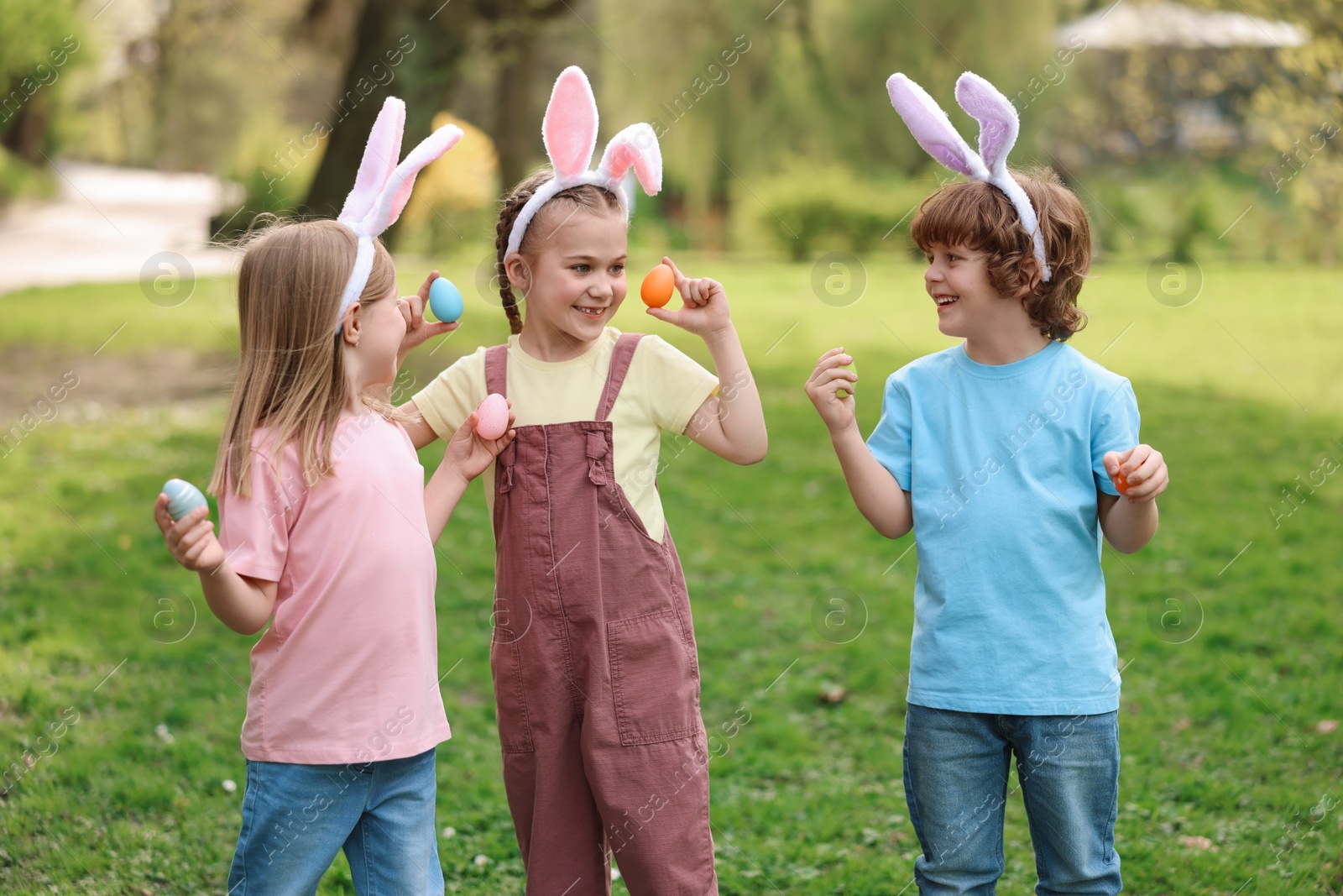 Photo of Easter celebration. Cute little children in bunny ears holding painted eggs outdoors