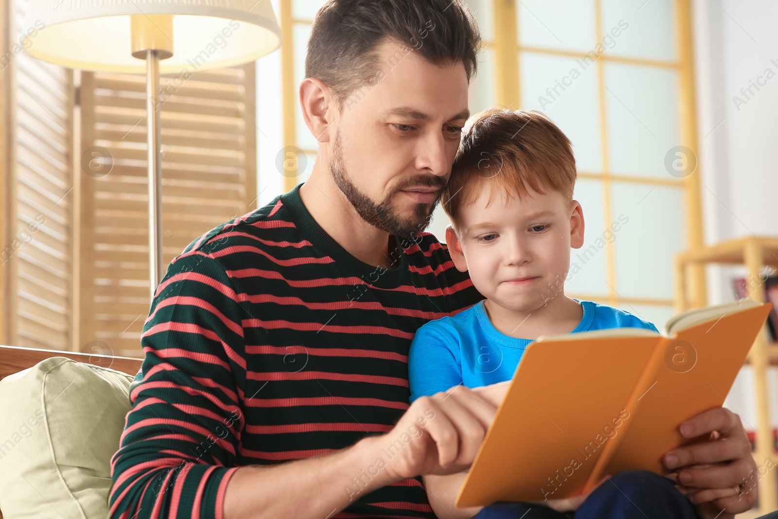 Photo of Father reading book with his son on armchair in living room at home