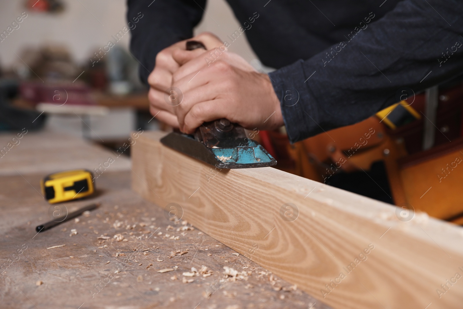 Photo of Professional carpenter grinding wooden plank with jack plane in workshop, closeup