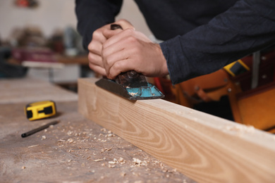 Photo of Professional carpenter grinding wooden plank with jack plane in workshop, closeup