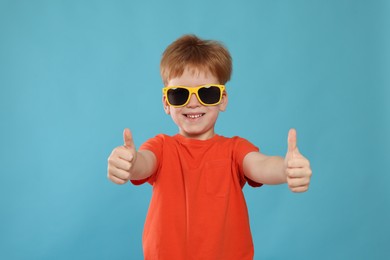 Cute little boy with sunglasses on light blue background