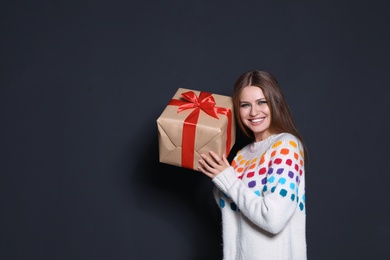 Photo of Young woman with Christmas gift on dark background. Space for text