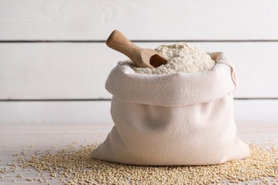 Photo of Sack with quinoa flour, scoop and seeds on white wooden table