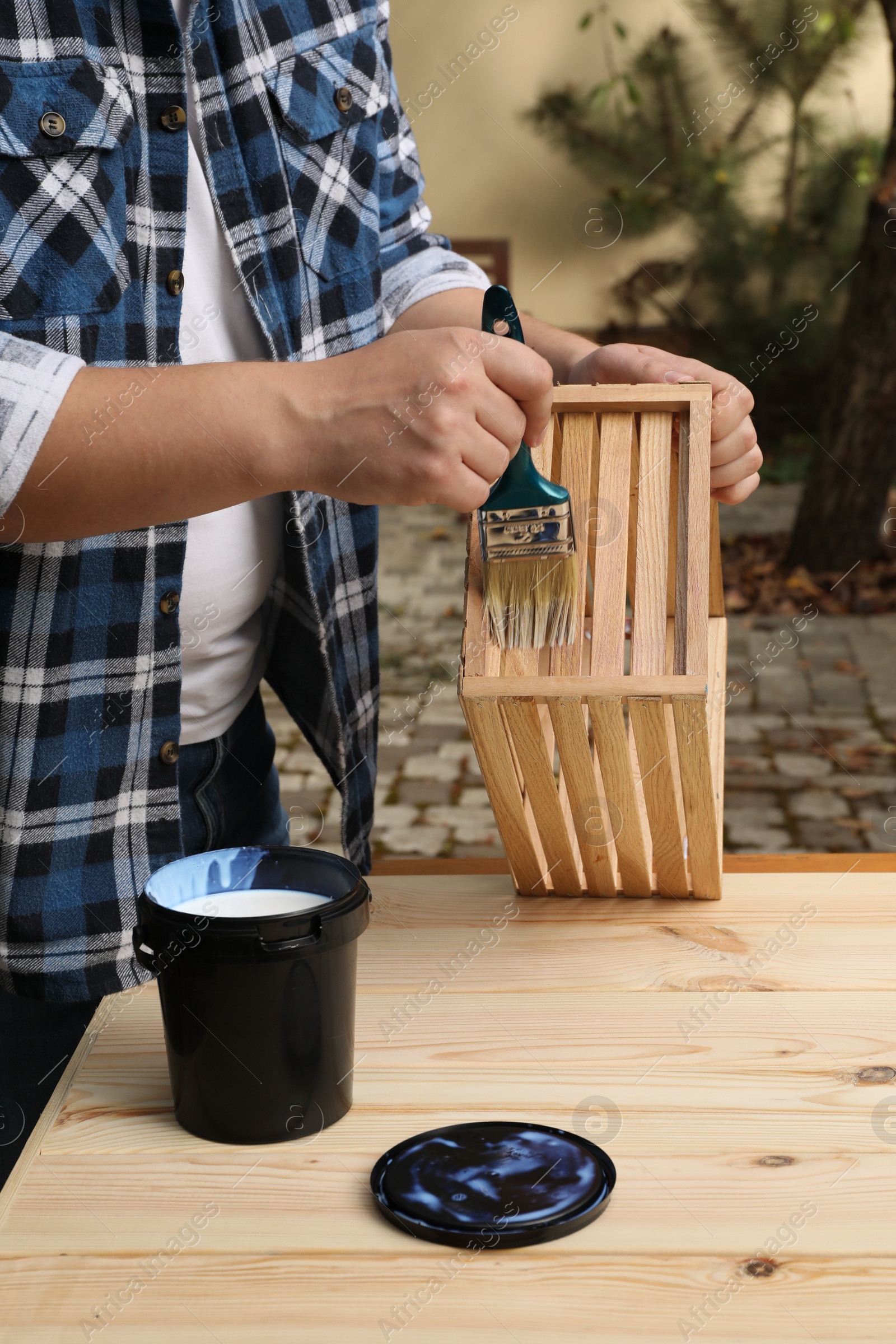 Photo of Man applying varnish onto wooden crate at table outdoors, closeup