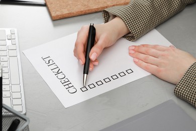 Photo of Woman filling Checklist at light grey table, closeup